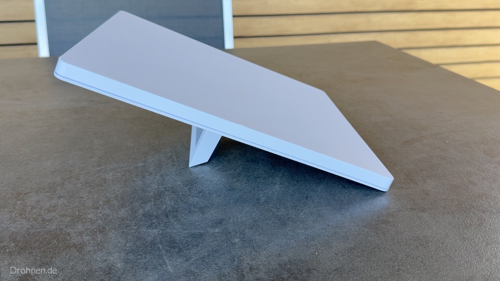 Starlink Mini steht mit ausgeklapptem Standfuß schräg auf einer Tischplatte.