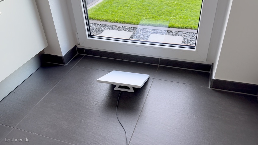 Starlink Mini mit angeschlossenem Kabel auf dem Fliesenboden direkt vor einer geschlossenen Glastür zum Garten.