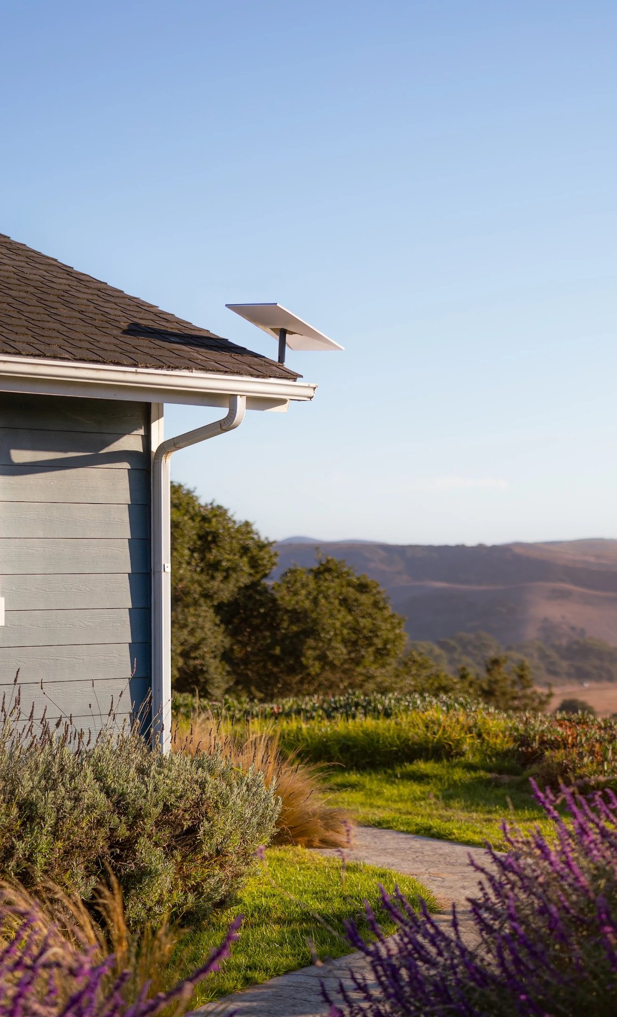 Hochformat eines Hauses mit Starlink-Terminal an der Dachkante und sonniger Landschaft.