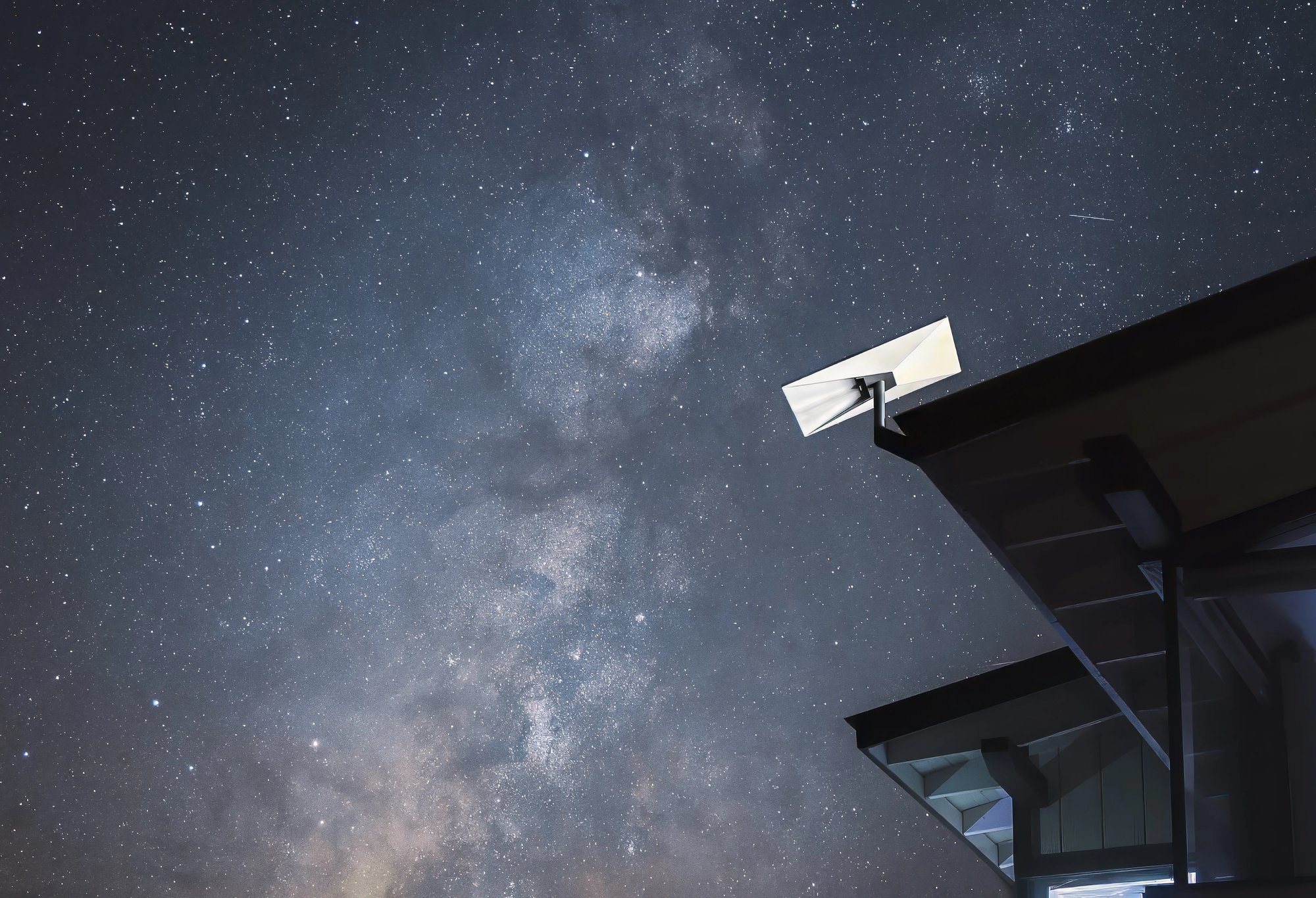 Starlink-Terminal an der Dachkante eines Hauses unter einem sternreichen Nachthimmel.