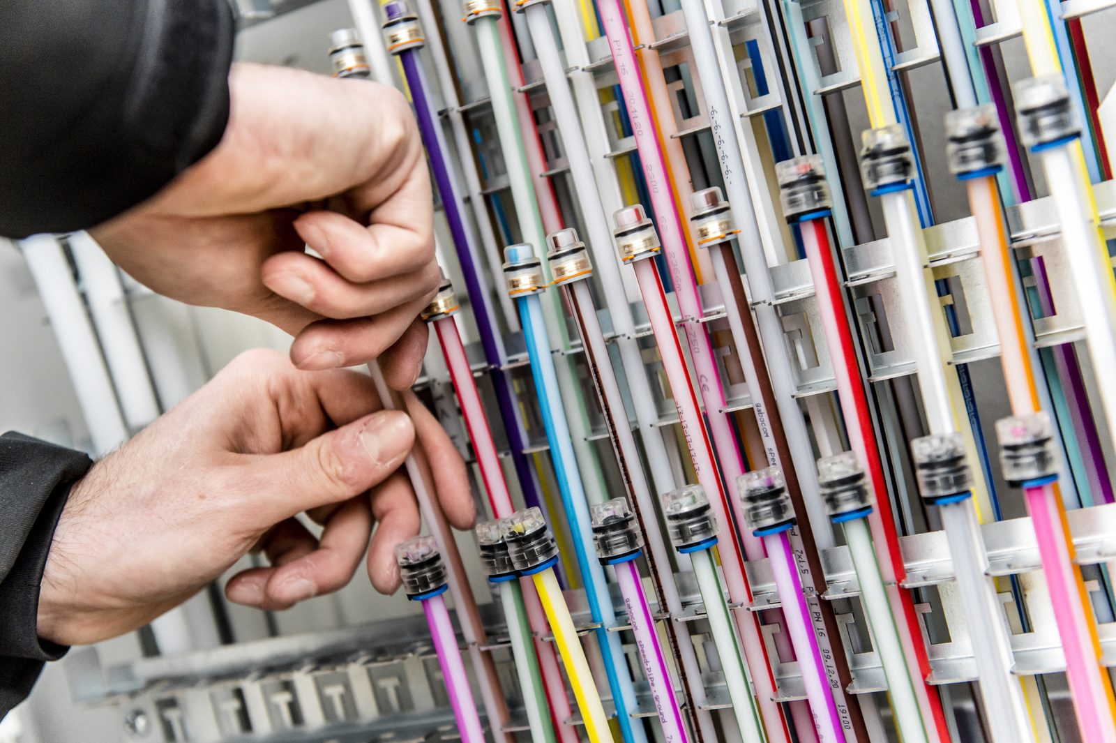 Hände sortieren bunte Mikrorohre in einem Glasfaser-Netzverteiler