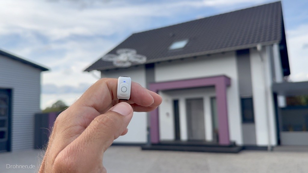Ring Remote zwischen den Fingern vor dem Haus, bereit zum Start
