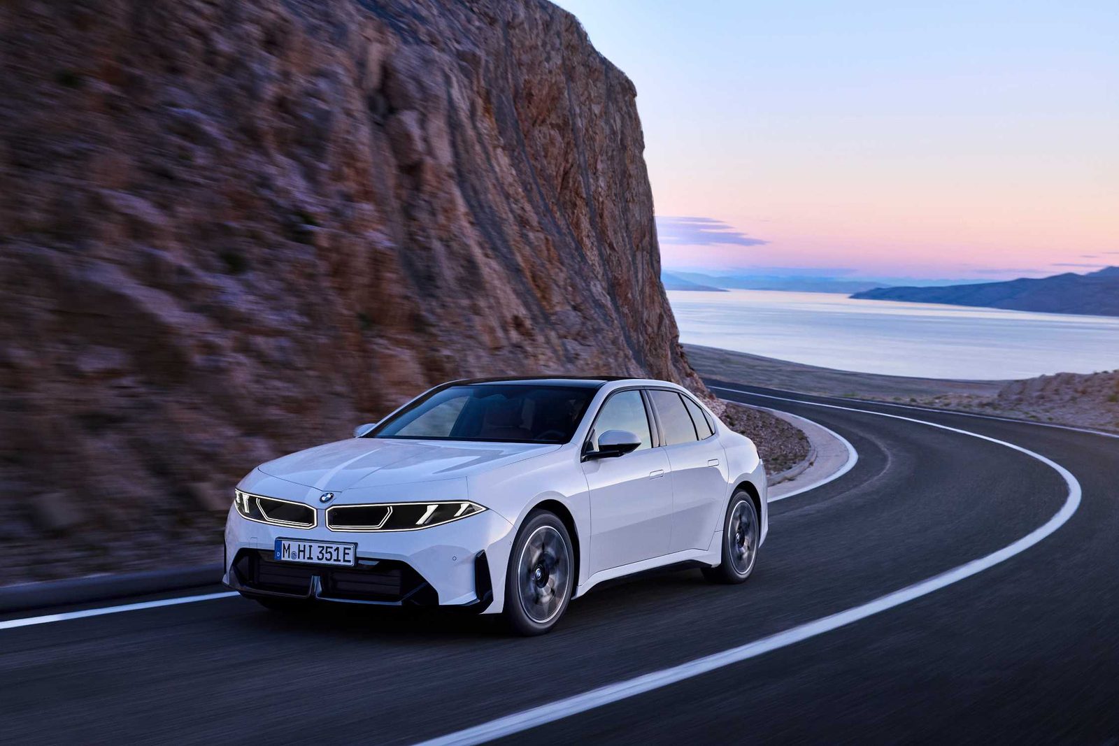 Weißer BMW i3 50 xDrive First Edition in einer Kurve an einer Felsküste in der Dämmerung