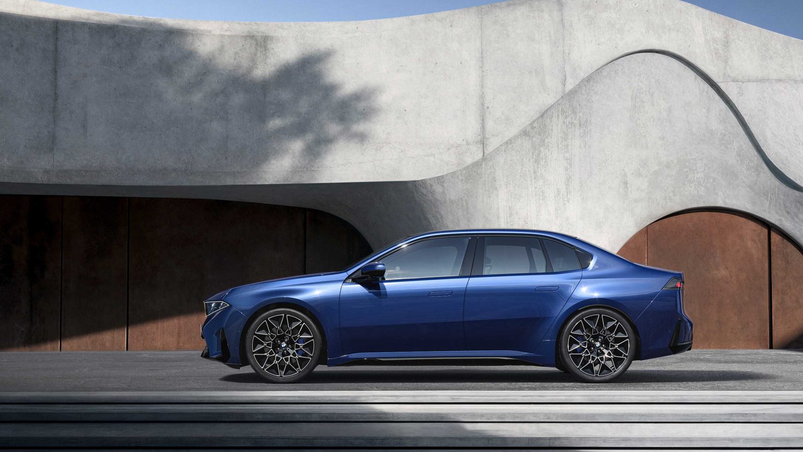 Seitenansicht des blauen BMW i3 50 xDrive vor einer geschwungenen Betonarchitektur