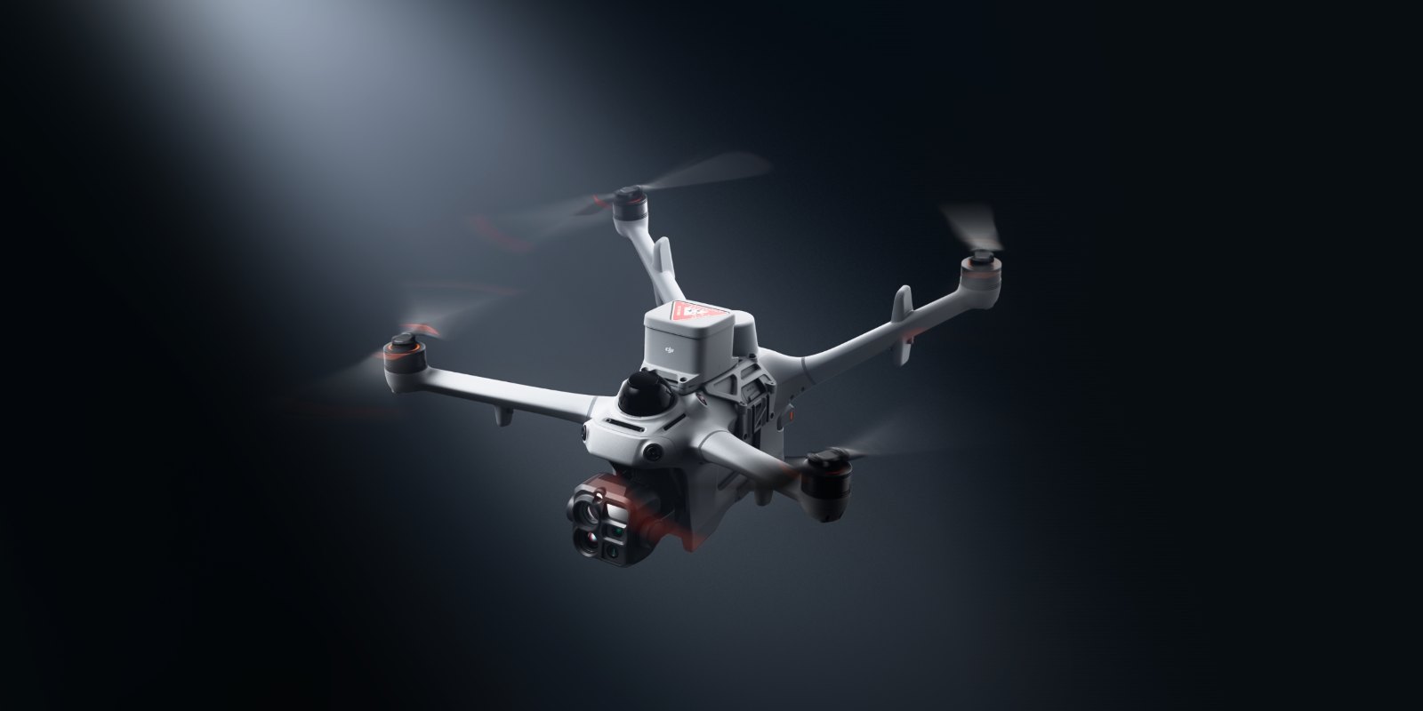 DJI Matrice 5TD mit Kameragimbal im Flug vor dunklem Hintergrund, angestrahlt von einem Lichtkegel