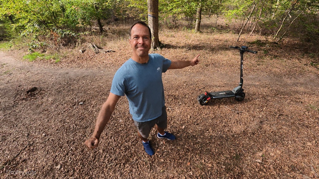 Tester zeigt auf den abgestellten iScooter iX7 Pro auf einer Waldlichtung