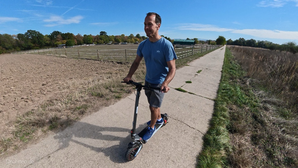 Fahrer auf dem iScooter iX7 Pro auf einem Feldweg, Vorderrad und Lenker im Vordergrund