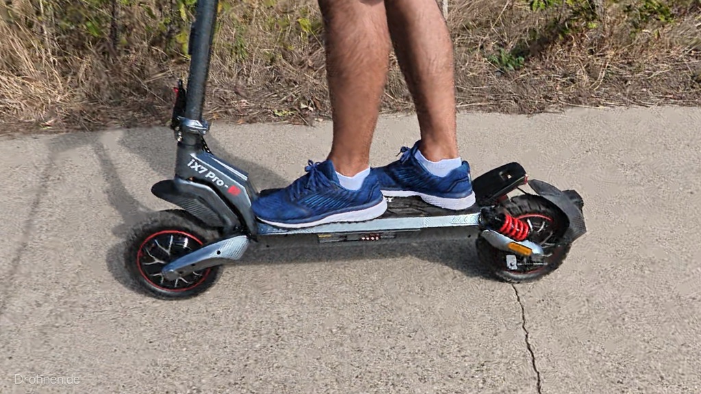 iScooter iX7 Pro von der Seite auf einem Betonweg, beide Füße auf dem Trittbrett