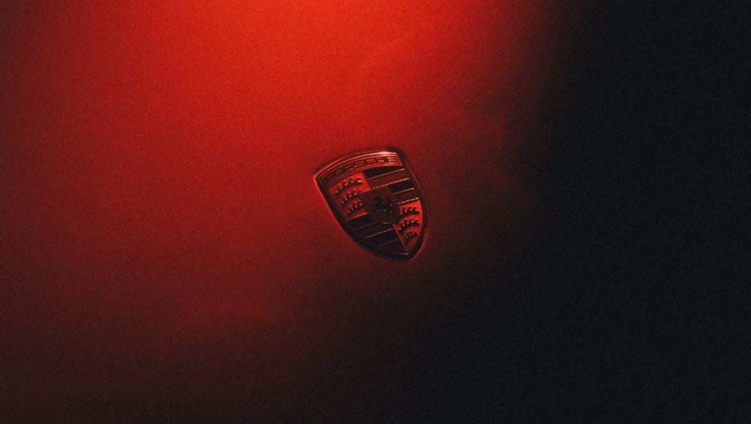 Porsche-Wappen im roten Licht auf dunklem Hintergrund im offiziellen Mission-S-Teaser