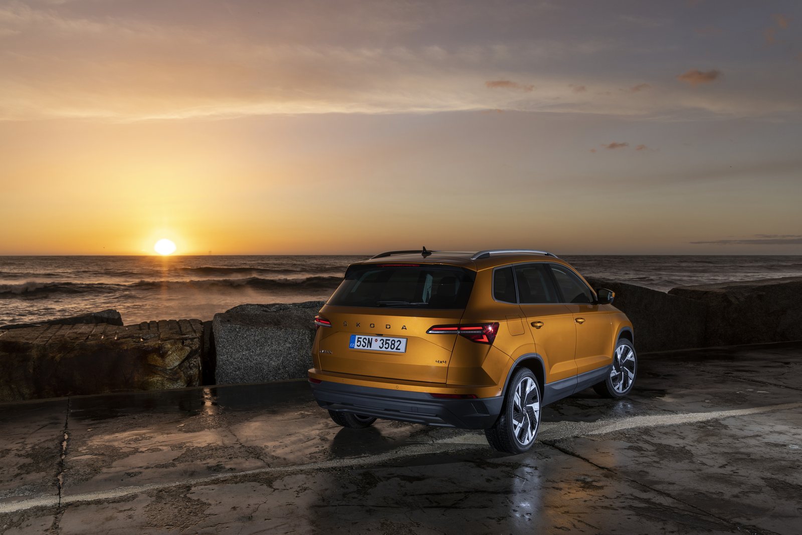 Orangefarbener Škoda Karoq in schräger Heckansicht am Meer bei Sonnenuntergang