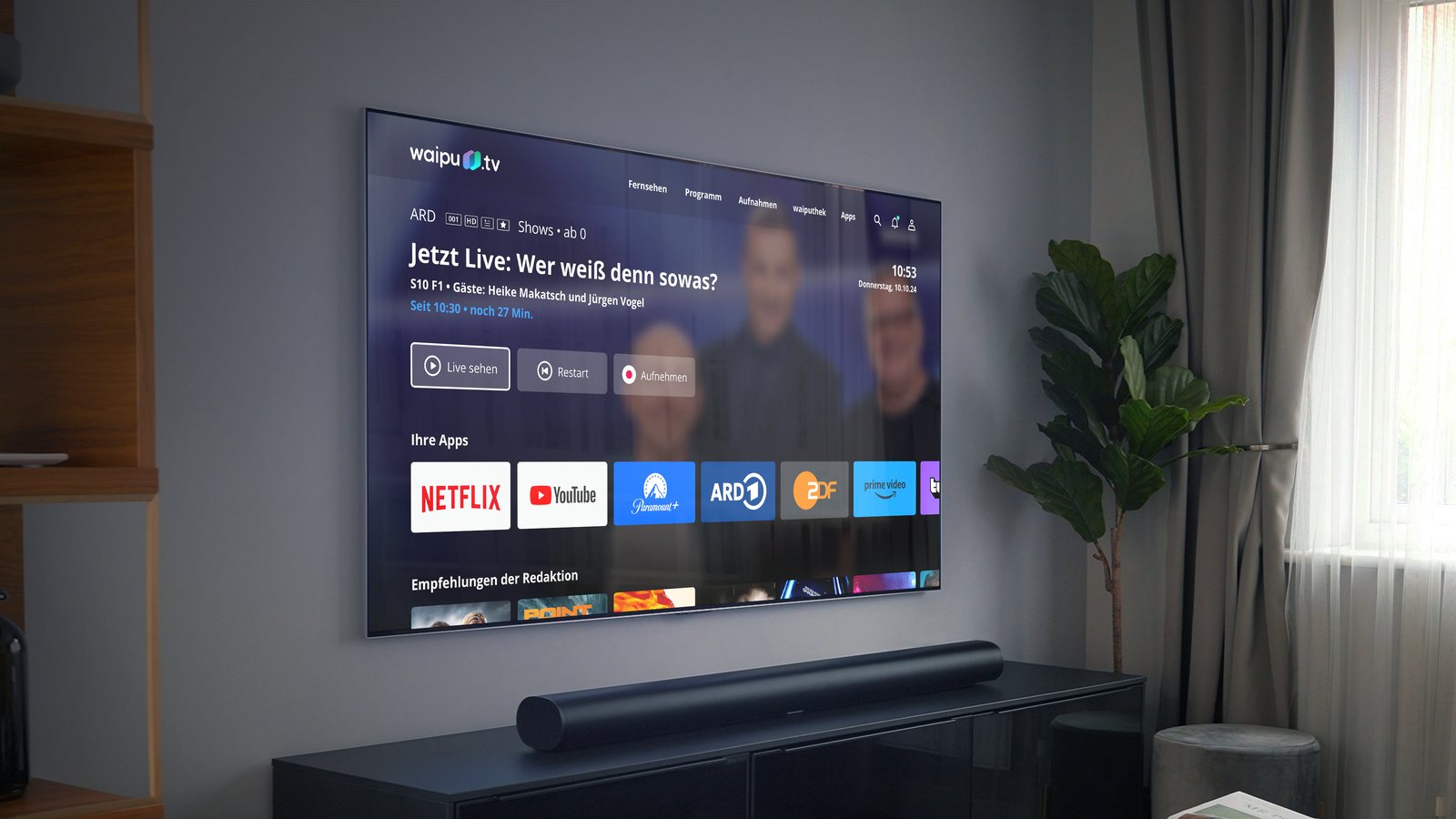 Fernseher an einer grauen Wand im Wohnzimmer mit der Bedienoberfläche von waipu.tv, darunter eine Soundbar